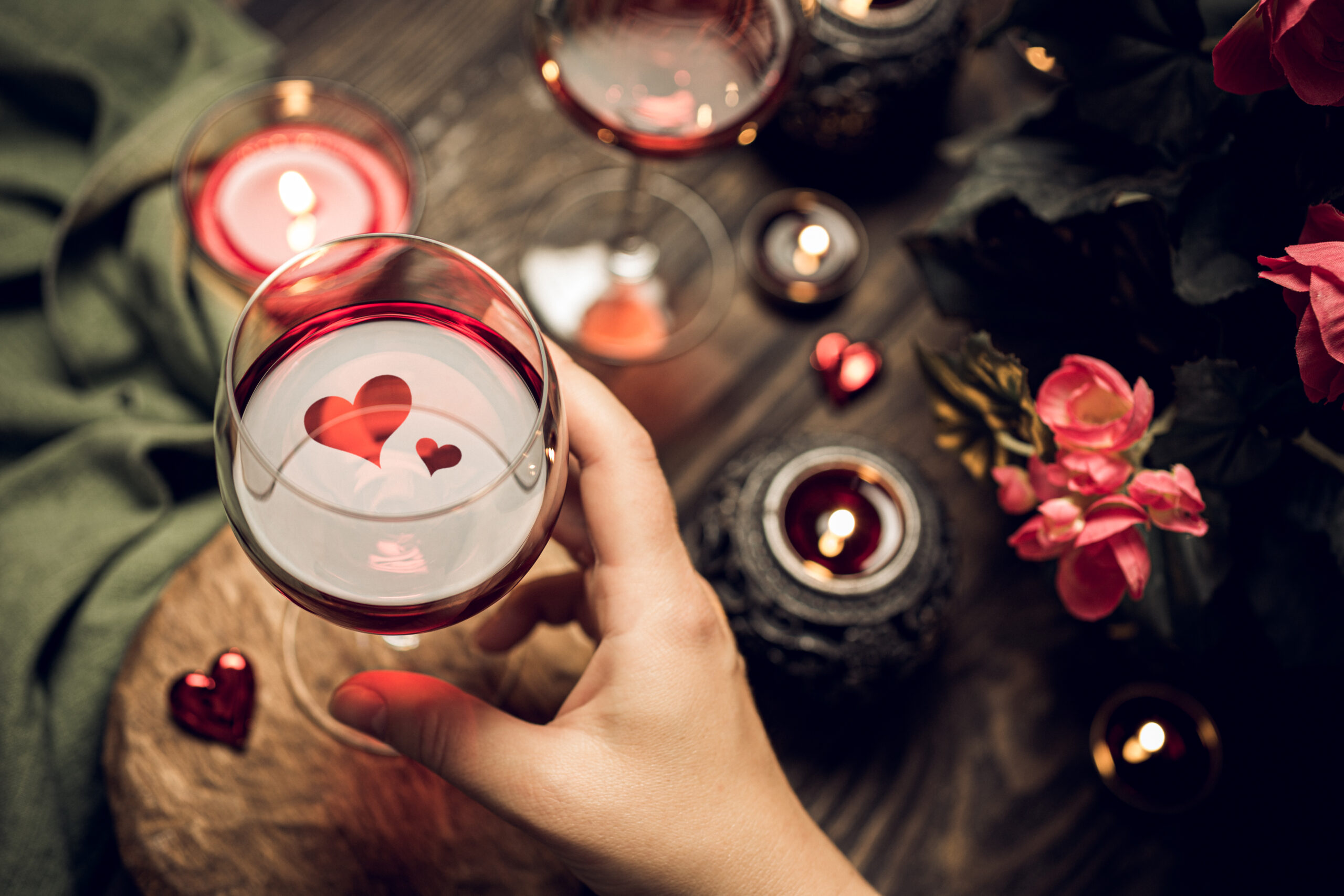 Romantic still life with red wine in glass and candles. Valentine's day concept greetinds card. Heart shape reflected in wine